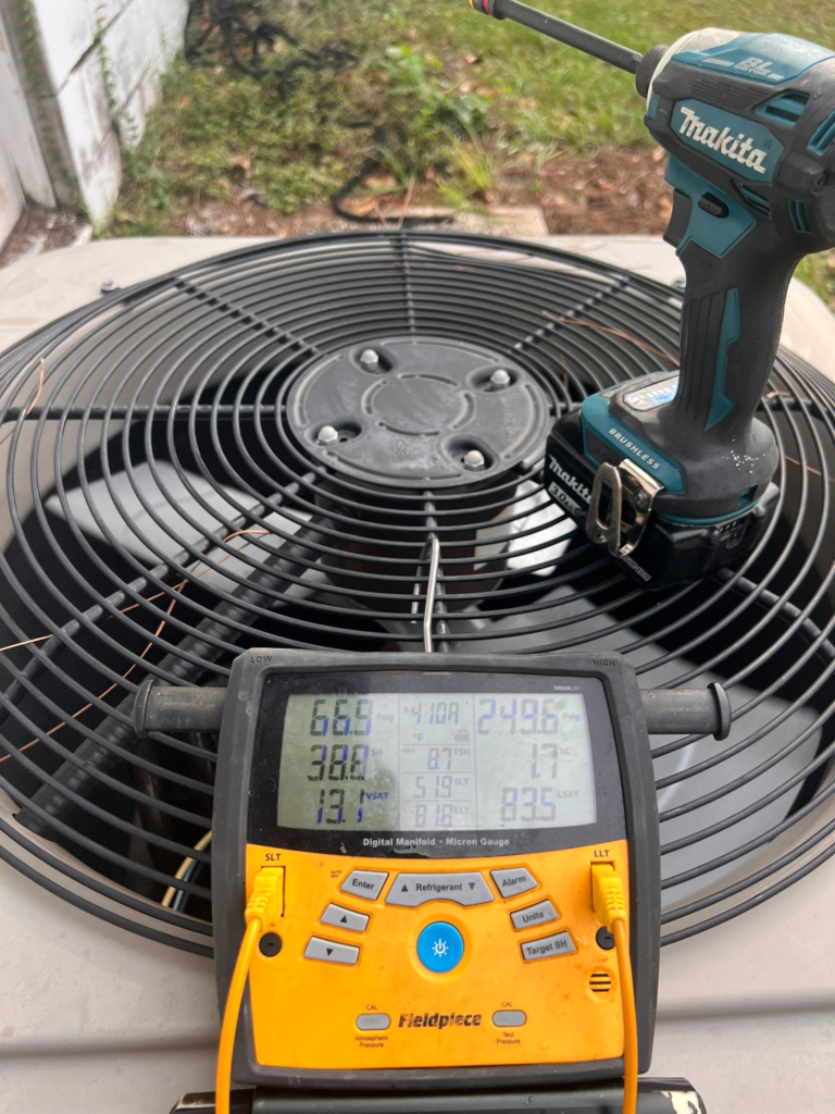 Top of outdoor AC condenser with diagnostic gauge and Makita drill during service check